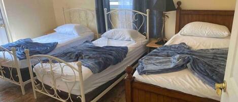 Ein Zimmer mit zwei Betten, eines mit weißem Metallgestell und das andere mit Holzgestell, beide mit weißer Bettwäsche und blauen Decken.