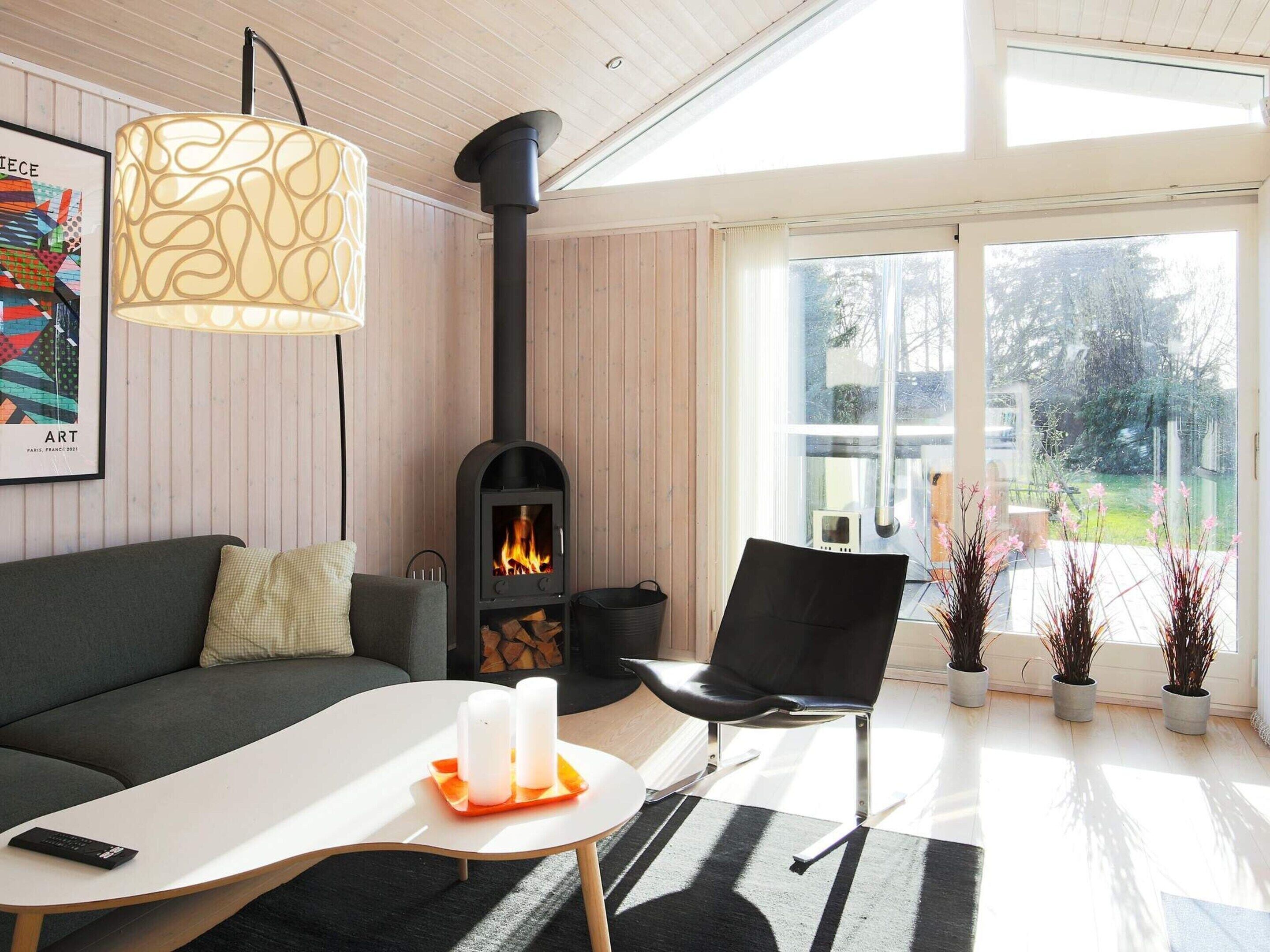 Ett modernt vardagsrum med en svart vedkamin, en grå soffa, ett vitt soffbord och en svart stol.