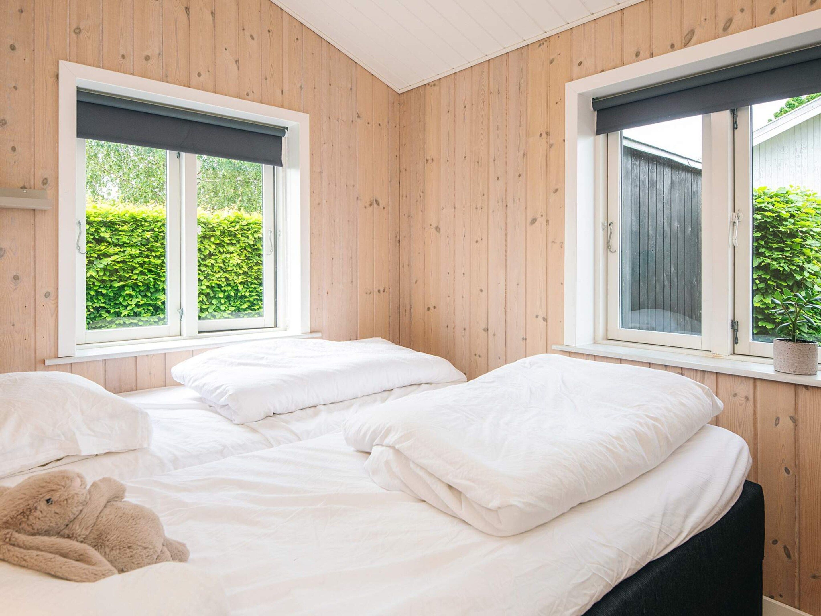 Quarto com duas camas, paredes de madeira e janelas com vista para o verde.
