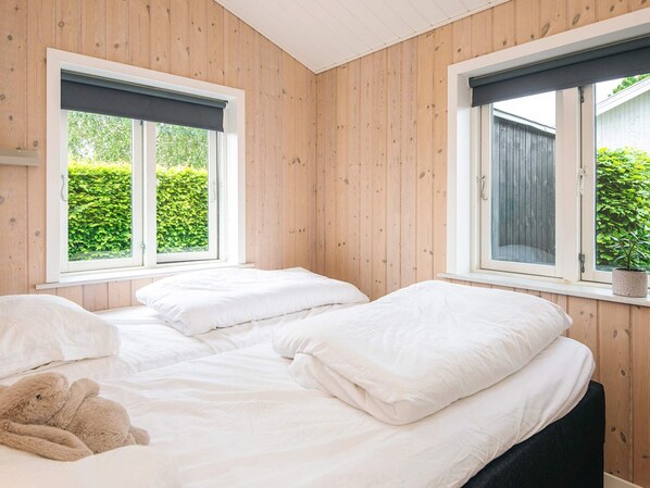 A room with two beds, wooden walls, and windows with views of greenery.