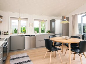 A modern kitchen with a dining area, featuring a round wooden table with black chairs, a built-in dishwasher, and a stainless steel refrigerator.