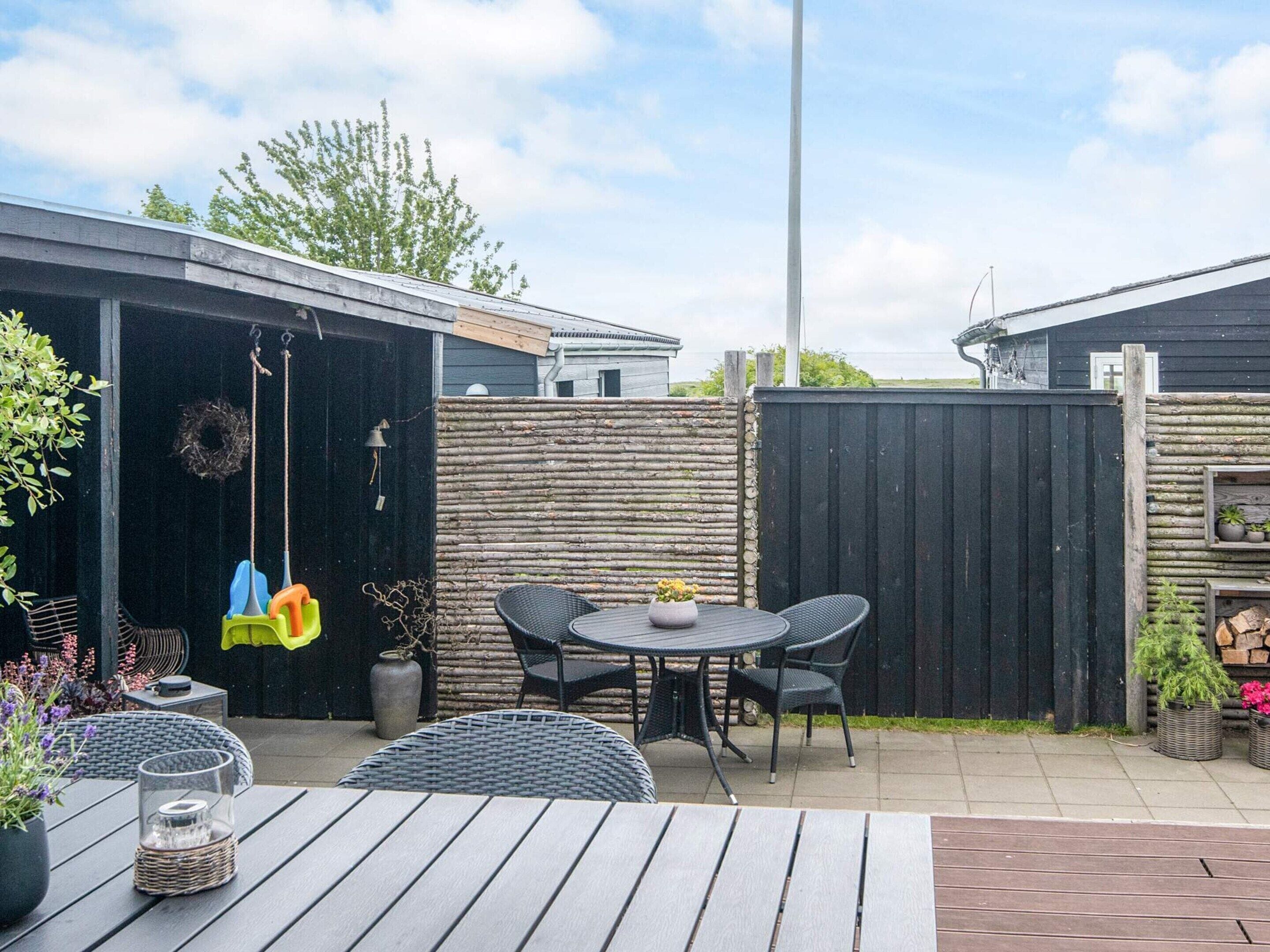 Eine Terrasse mit Tisch, Stühlen und einer Schaukel, sowie einer Zierwand.