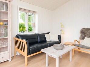 A living room with a black leather sofa, a white coffee table, and a wooden chair. There is a bookshelf with glass jars and a potted plant.