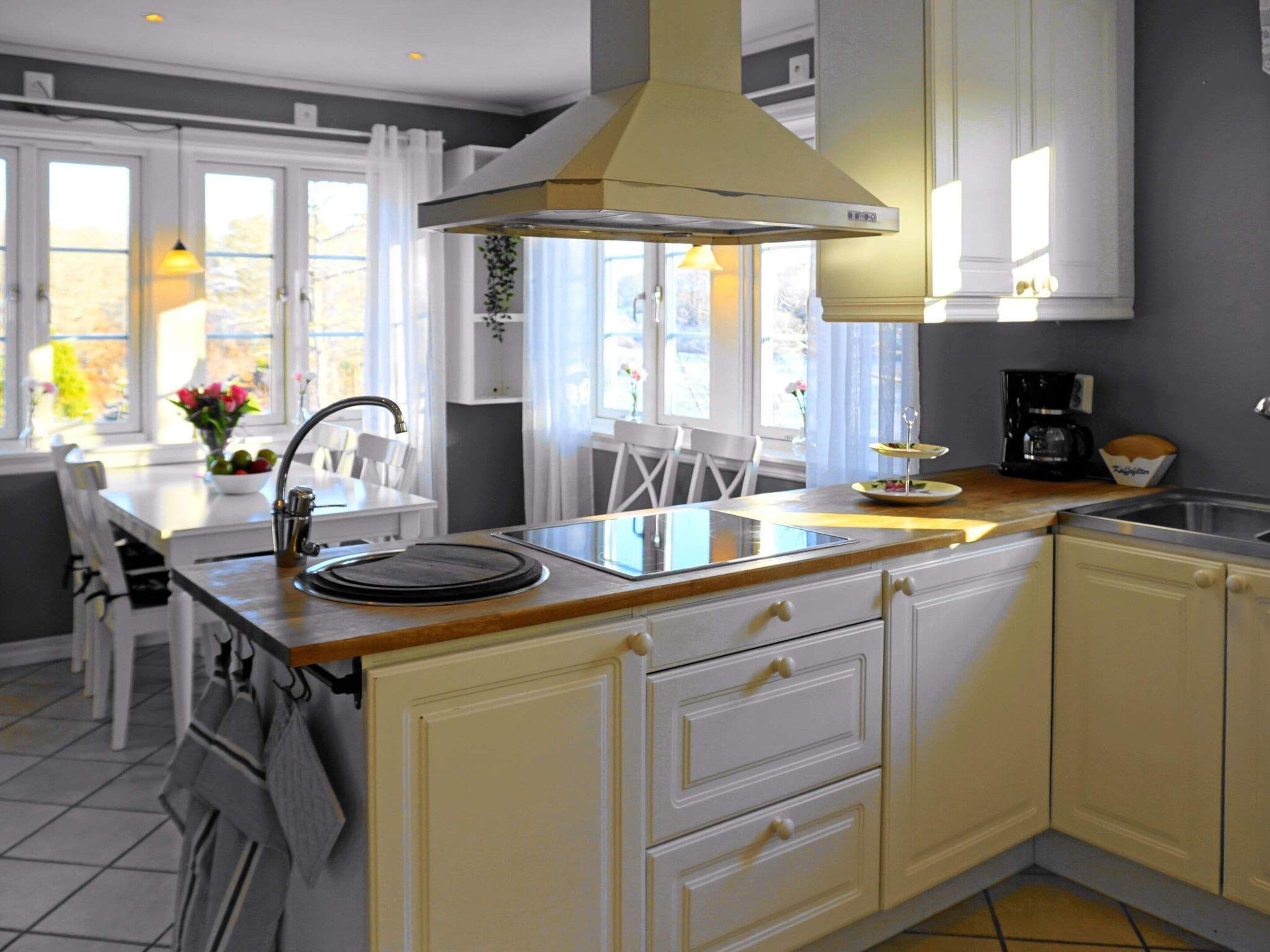 Une cuisine dotée d’un îlot central, de meubles blancs et d’une hotte de cuisinière moderne.