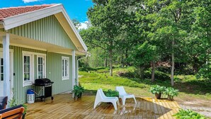 Een houten terras met twee witte stoelen, een barbecue en potplanten.