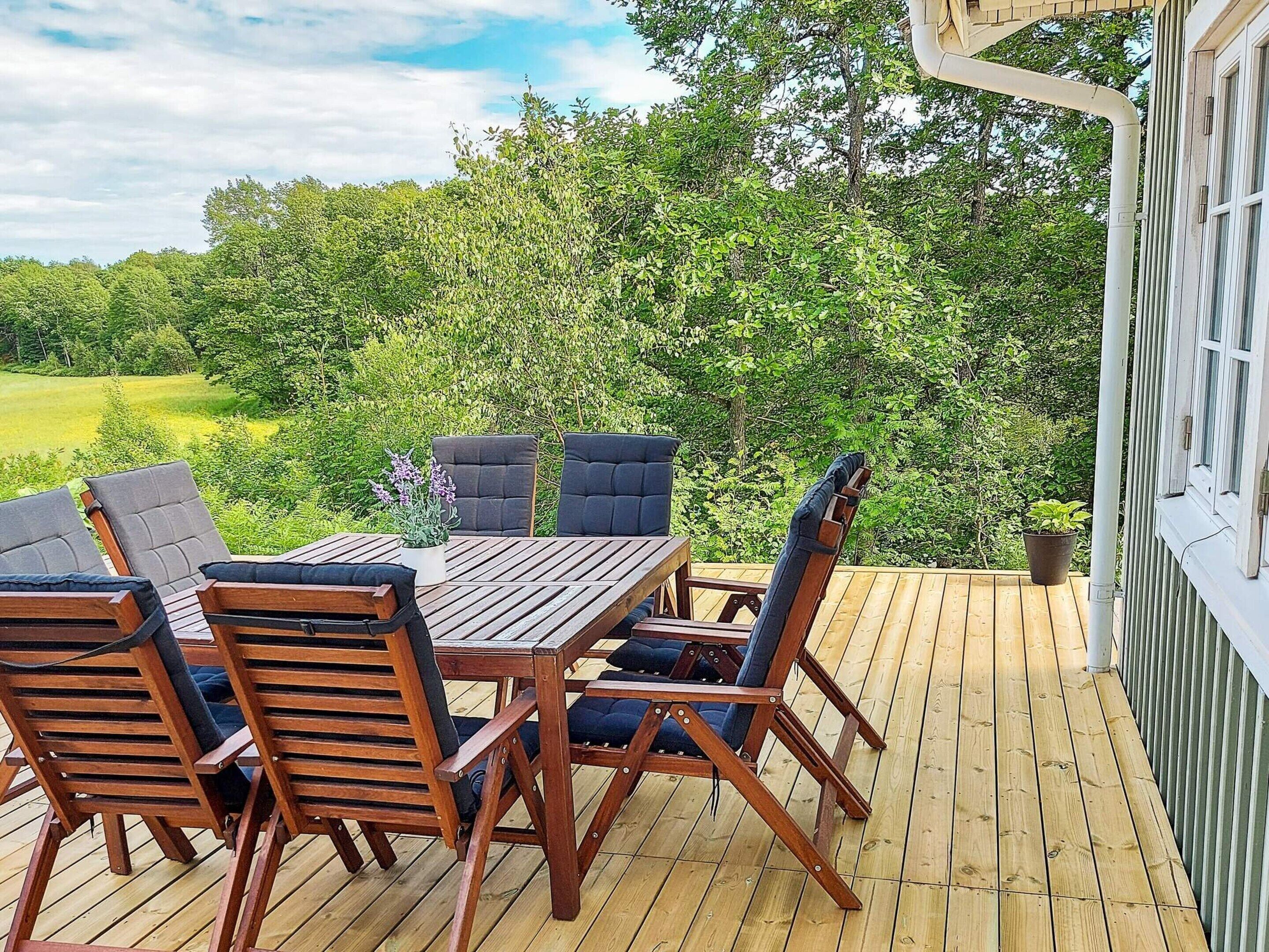 Een houten terras met een tafel en stoelen, omringd door weelderige begroeiing en bomen.