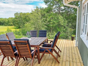 A wooden deck with a table and chairs, surrounded by lush greenery and trees. - 4 Star Holiday Home in Ellos (Ellos)