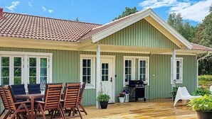 Een groene woning met een overdekte patio, een barbecue en een eethoek met houten stoelen en een tafel.