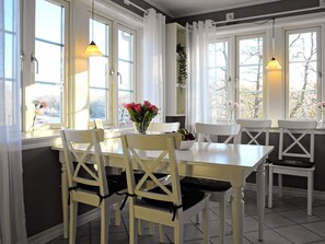 A dining area with a white table and chairs, large windows with curtains, and pendant lights. - 4 Star Holiday Home in Ellos (Ellos)