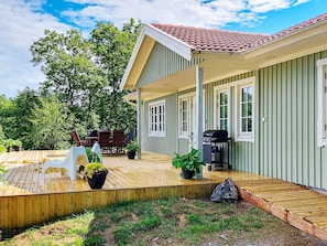 A covered outdoor area with a wooden deck, a barbecue grill, and potted plants. - 4 Star Holiday Home in Ellos (Ellos)