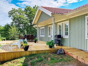 A covered outdoor area with a wooden deck, a barbecue grill, and potted plants. - 4 Star Holiday Home in Ellos (Ellos)