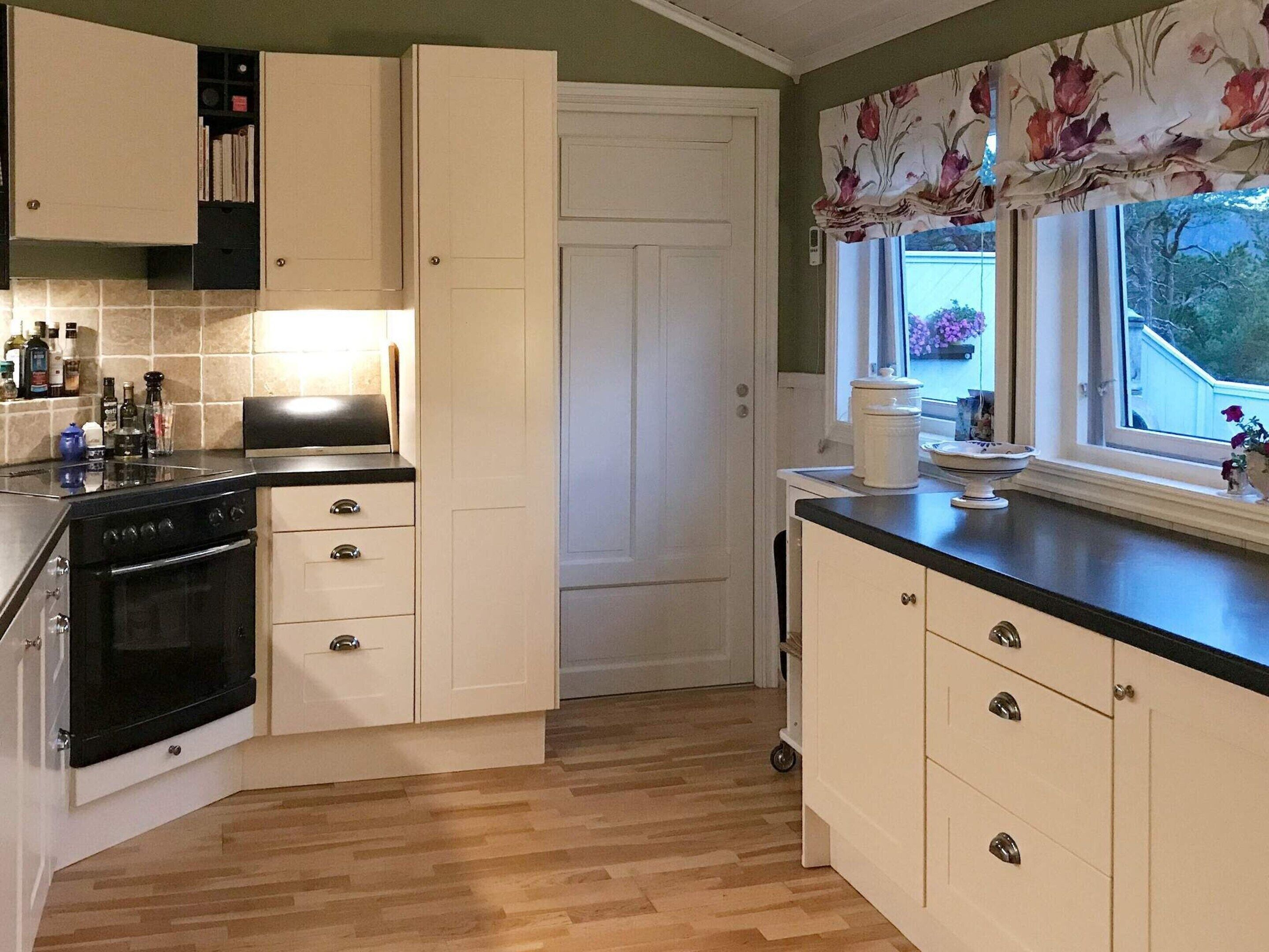 A kitchen with a black stove, white cabinets, and a window with a view of greenery outside.