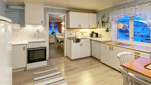 A compact kitchen with white cabinets, a stove, and a sink. There is a dining area with a table and chairs, and a window with a view of a snowy landscape. - 8 Person Holiday Home in Stonglandseidet (Senja)