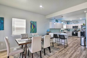 A modern kitchen with white cabinets, a central island, and a dining area with a wooden table and chairs. - Gulf-View Home w/ Dog Run in Surfside Beach! (Surfside Beach)
