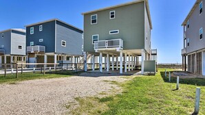 A row of beach houses with balconies, a gravel driveway, and a grassy area.