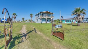 A large house with a balcony, surrounded by a grassy area and palm trees. - Waterfront Texas Abode w/ Boat Ramp, Pets Welcome (Sargent)