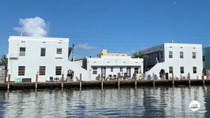 A waterfront building with a dock, featuring a central structure with a flat roof and two side wings.