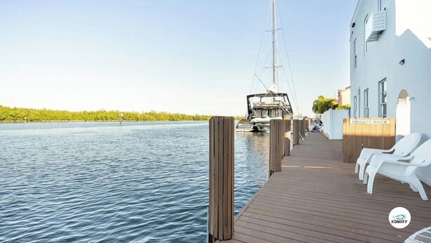 A wooden dock with white lounge chairs, a private dock sign, and a sailboat in the background.