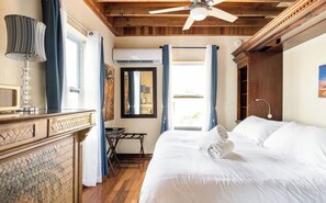 Un dormitorio con cama, ventilador de techo, escritorio y ventana con cortinas.