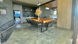 Una cocina moderna con una mesa de comedor de madera, sillas negras de alambre y una lámpara colgante.
