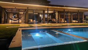 Un área de piscina moderna al aire libre con zona de estar cubierta, una hamaca y un bar junto a la piscina.