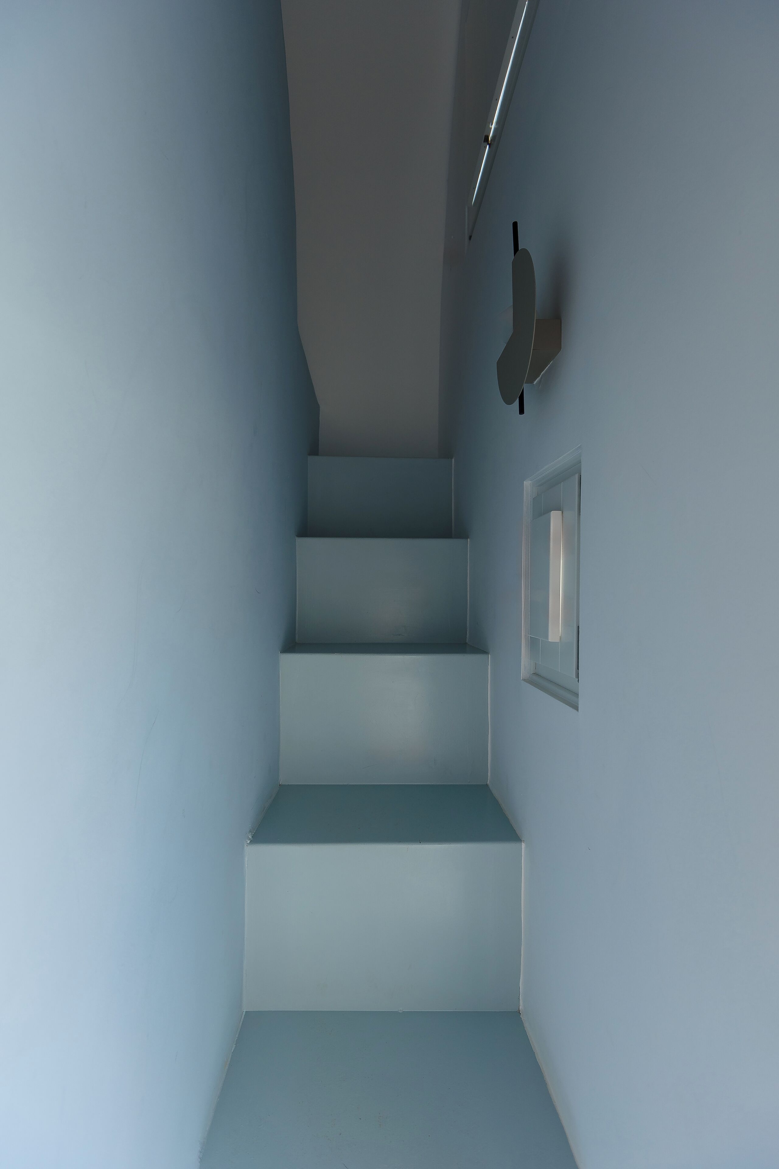 Eine Treppe mit blauer Wand, einem kleinen Fenster und einer Leuchte.