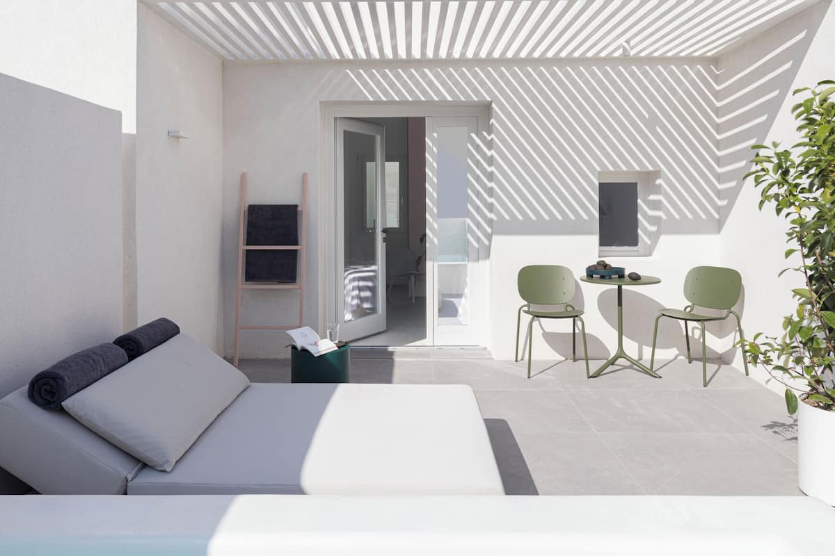 A modern outdoor pool area with a sun lounger, a small table with chairs, and a potted plant.