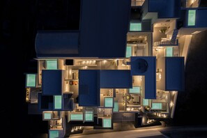 A modern, multi-level hotel with distinct geometric shapes and illuminated interior spaces. - Neo Suites (Santorini)