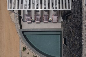 An aerial view of a rooftop pool area with lounge chairs and a stone wall. - Neo Suites (Santorini)