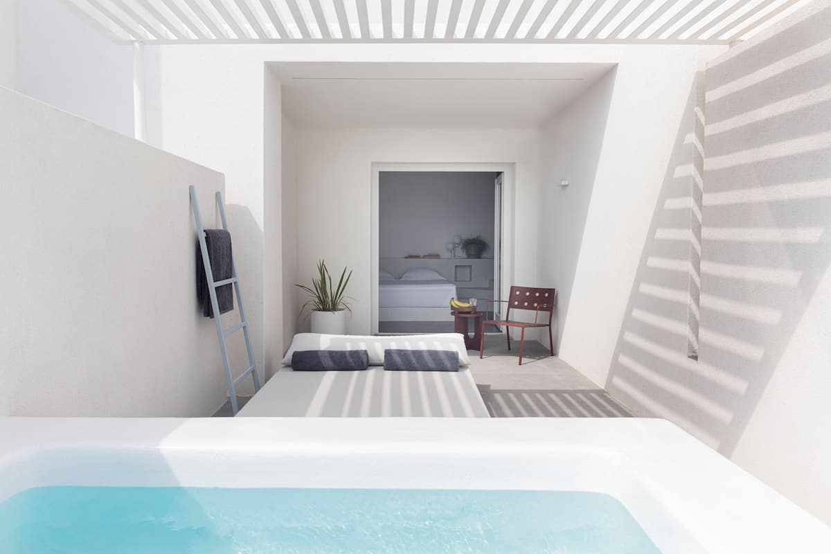 A modern, minimalist bedroom with a large bed, a small desk, and a view into a bathroom.