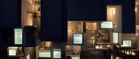 A modern building with multiple illuminated rooms and balconies, featuring a contemporary architectural design.