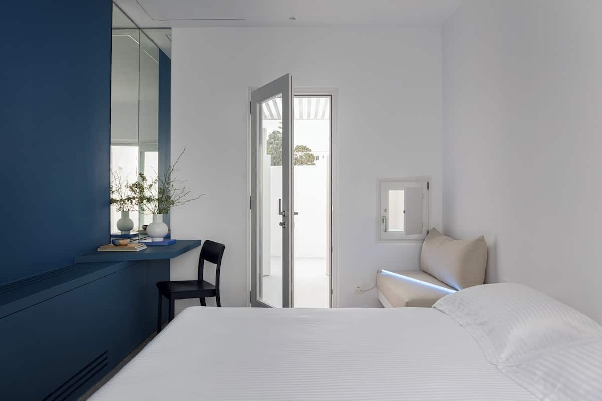 A bedroom with a bed, a chair, a desk, a window, and a door.