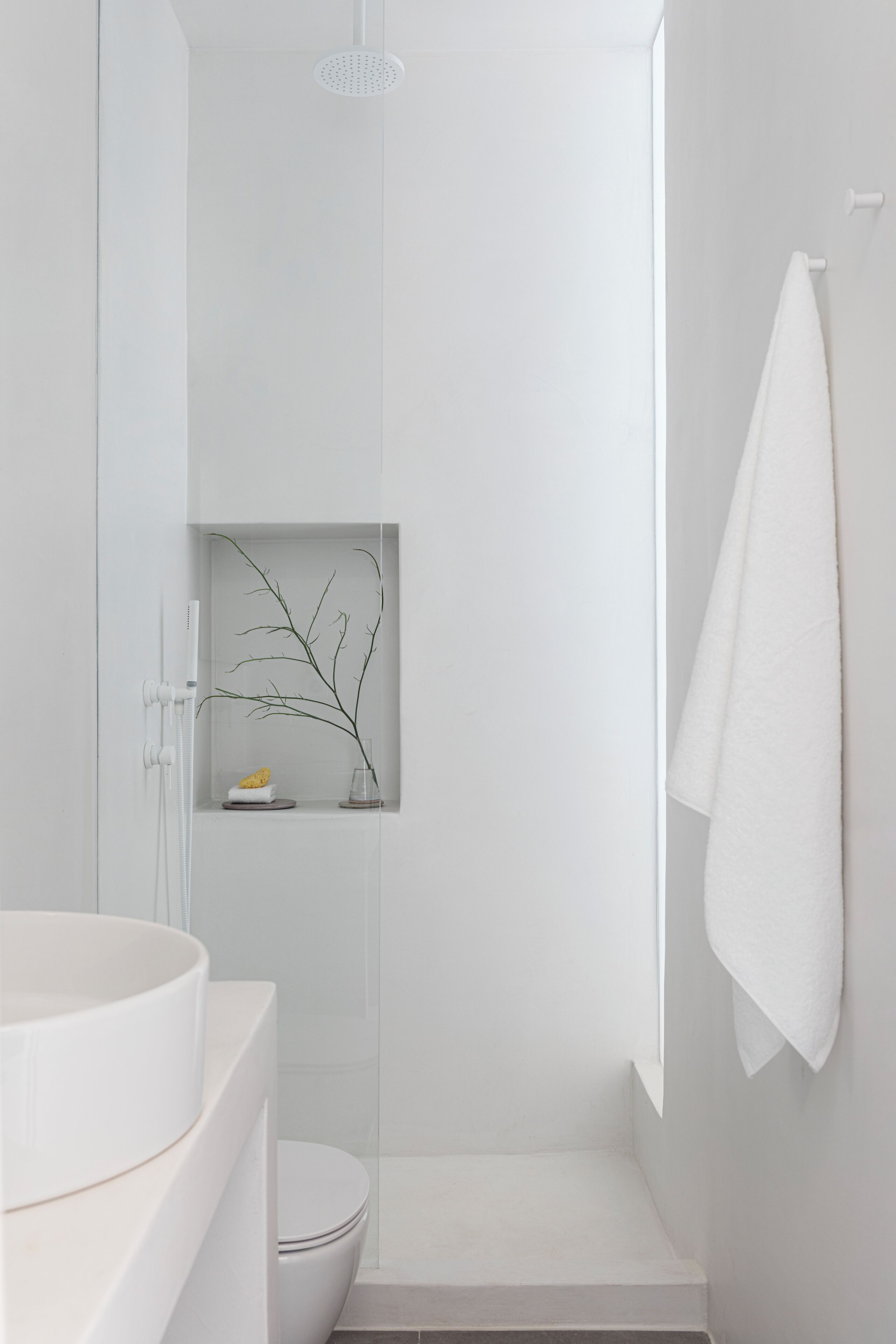 Un baño moderno con lavamanos, inodoro y zona de ducha blancos.