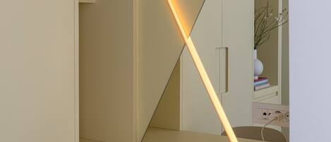 A modern desk with a lighted desk lamp, a white chair, and a shelf with a brown vase.