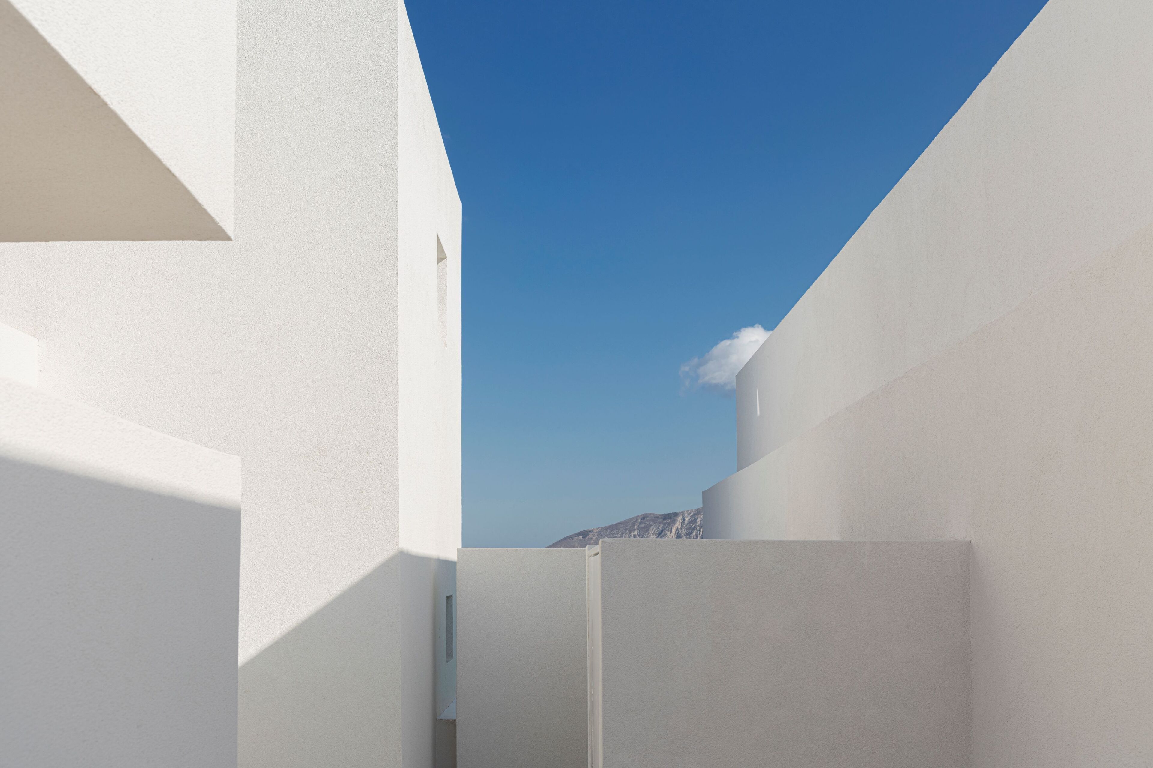A narrow, white-walled corridor with a clear blue sky above.