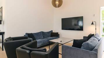A modern living room with a sectional sofa, a coffee table, and a flat-screen TV mounted on the wall.