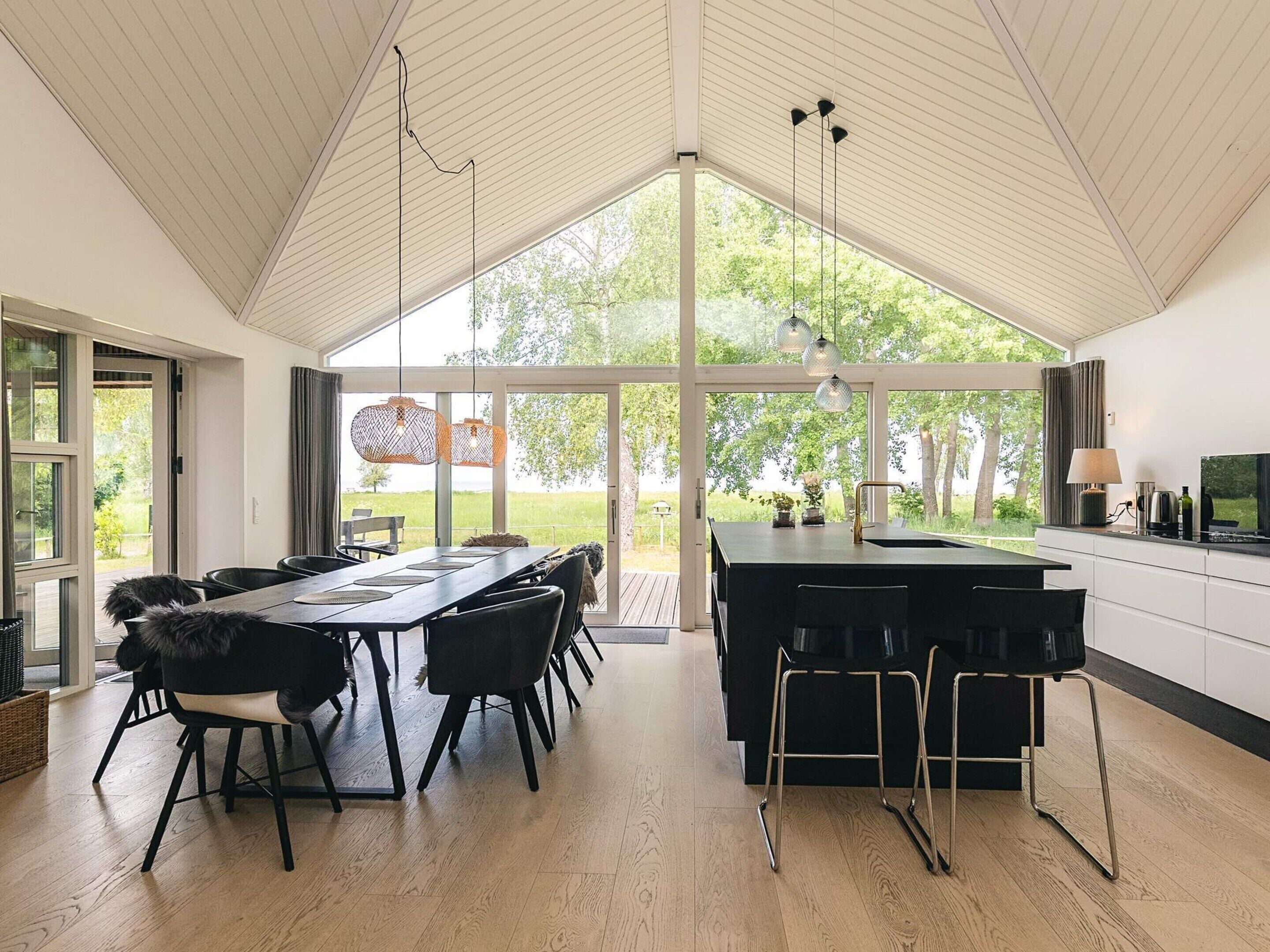 A modern kitchen with a large island, black bar stools, and a dining area with a wooden table and chairs.
