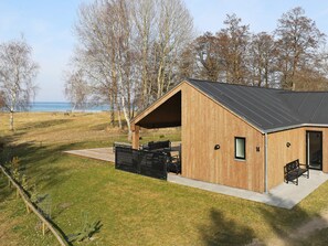 A wooden cabin with a covered patio, a view of the sea, and a fenced yard.