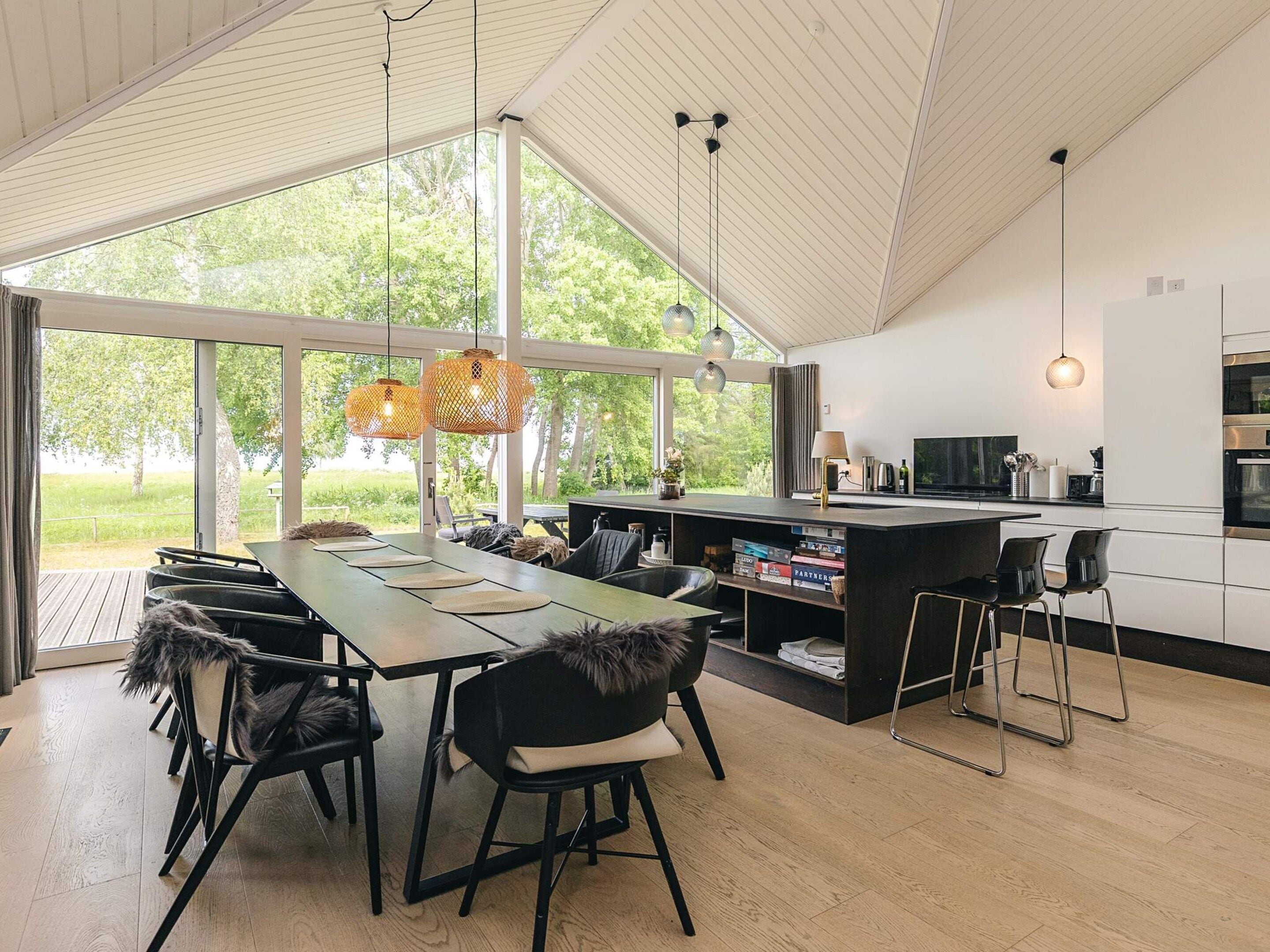 Cocina moderna con una isla grande, comedor con sillas y vistas a la vegetación.