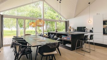 Cocina moderna con una isla grande, comedor con sillas y vistas a la vegetación.