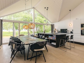 Cocina moderna con una isla grande, comedor con sillas y vistas a la vegetación.