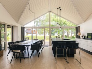 A spacious dining area with a large table and chairs, a kitchen with a sink and counter, and large windows offering a view of the outdoors. - 5 Star Holiday Home in Stroby (Strøby)