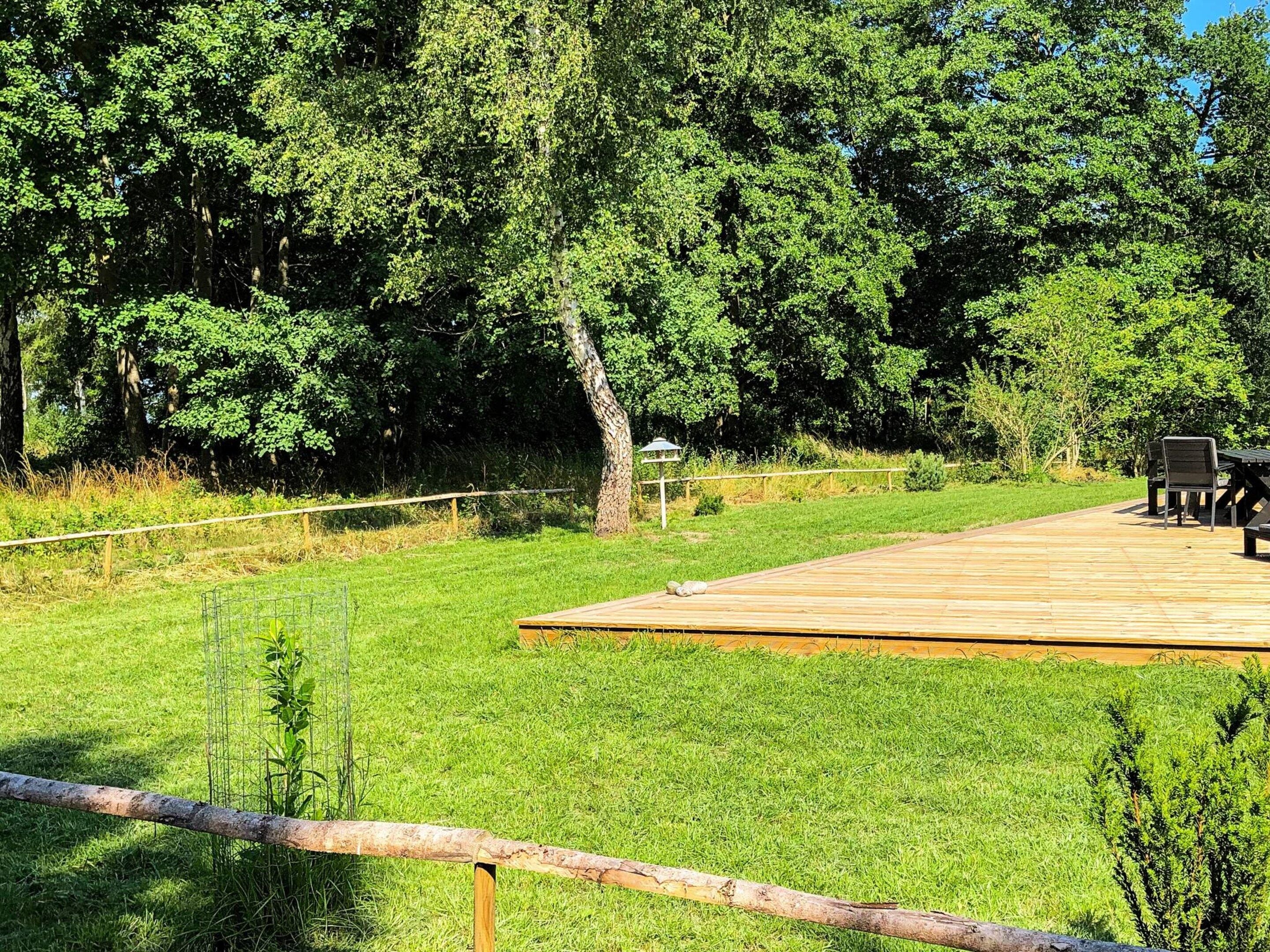 A wooden deck with outdoor seating, surrounded by a grassy area and trees.