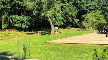 A wooden deck with outdoor seating, surrounded by a grassy area and trees.
