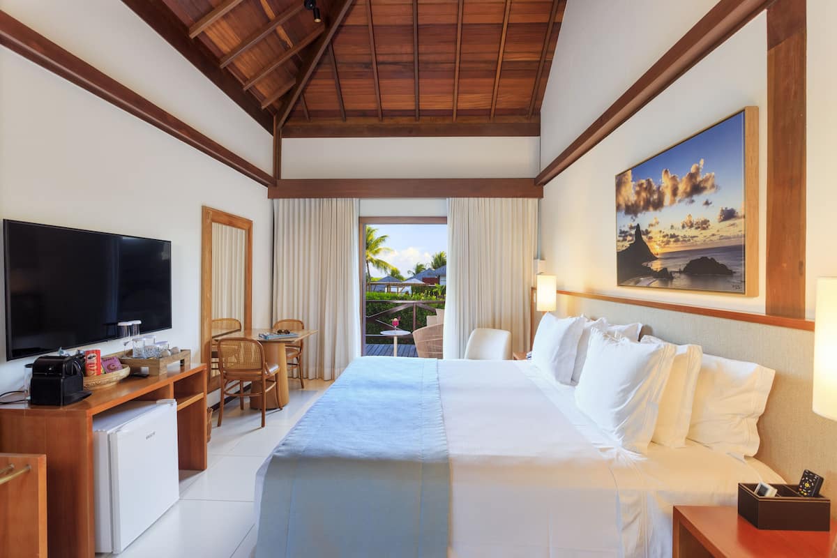 A hotel room with a large bed, a desk with a TV, a small fridge, and a view of the outdoors.