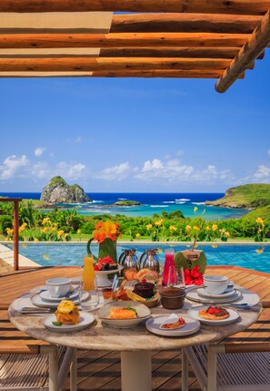 Ein Tisch ist für ein Frühstück gedeckt, mit Blick auf einen tropischen Strand und den Ozean.