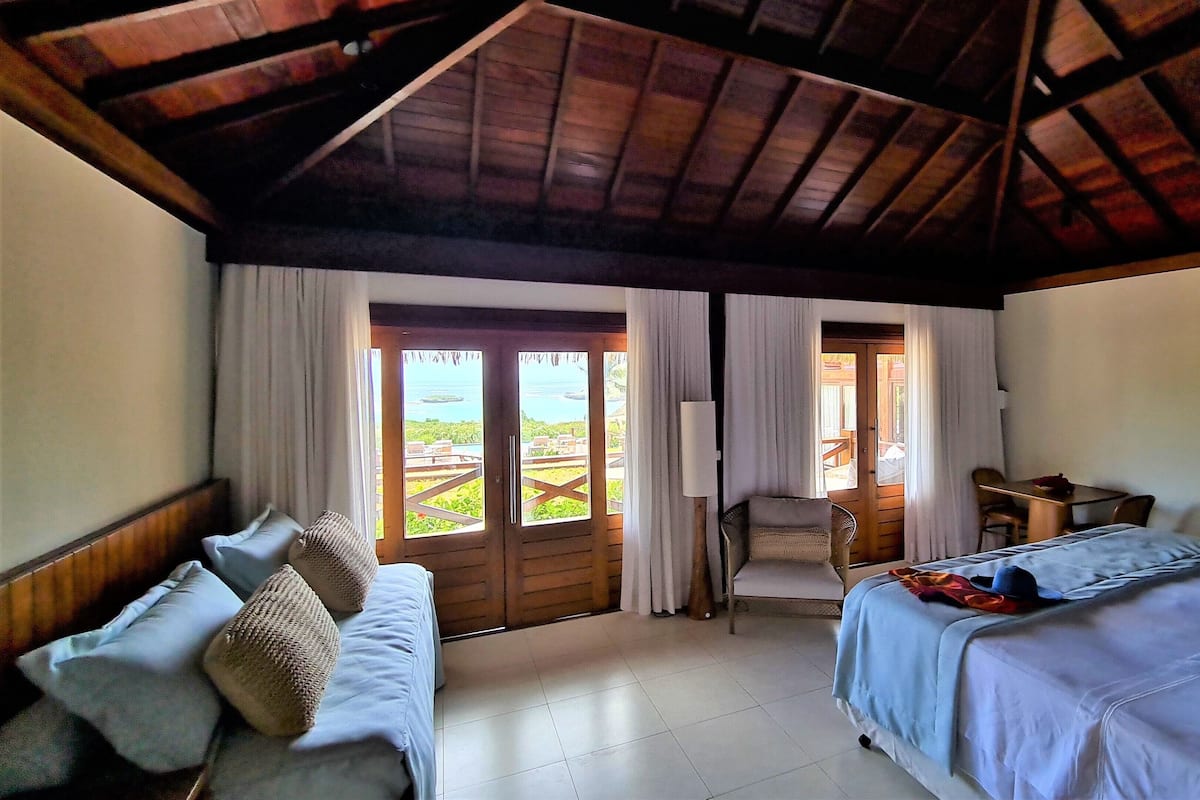 A hotel room with a wooden ceiling, a bed, a sofa, a desk, and a view of the outdoors.