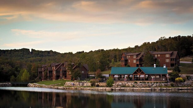 A lakeside lodge with multiple wooden buildings, a covered patio, and a stone wall.