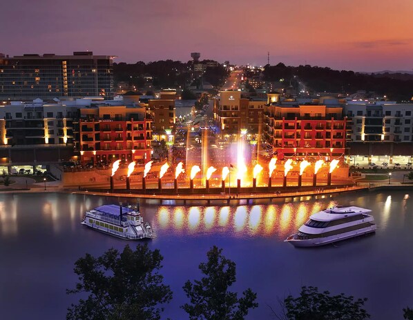 A waterfront hotel with a central fountain, two boats docked, and surrounding buildings.