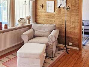 A room with a beige sofa, a matching ottoman, a floor lamp, a radiator, and a window with curtains. - 6 Person Holiday Home in Trollhattan (Trollhattan)